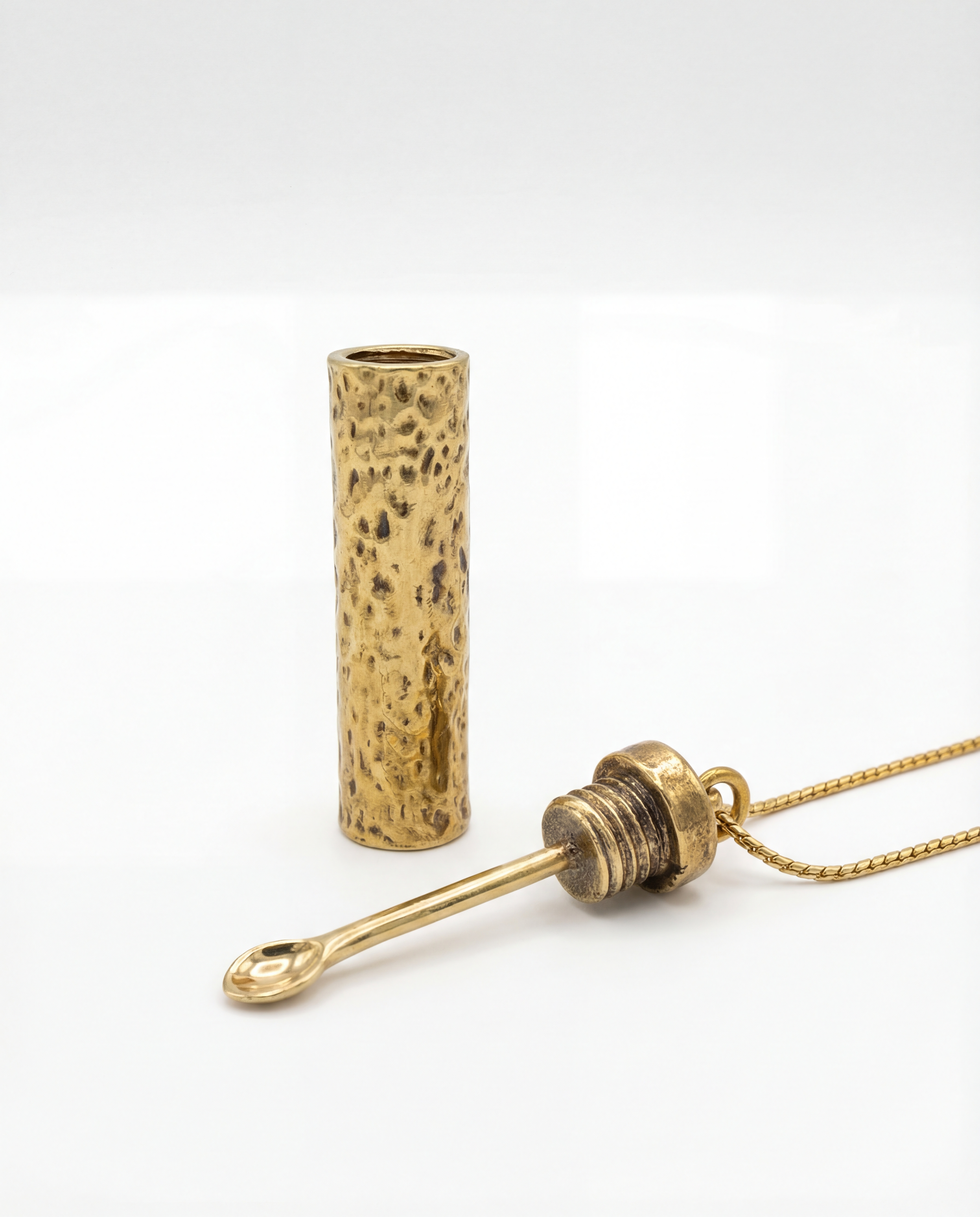 Gold necklace with a cylindrical pendant on a white background