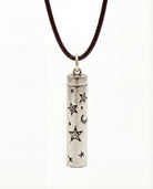 Silver cylindrical pendant with star and moon designs on a brown cord against a white background