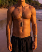 Man with a necklace standing on a beach at sunset