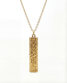 Gold cylindrical pendant necklace on a white background
